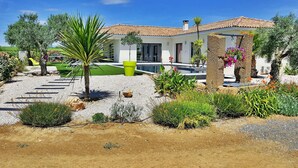 A modern house with a swimming pool, surrounded by a landscaped garden with various plants and a gravel driveway.