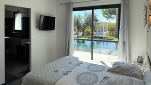 A bedroom with a bed, a TV, and a view of a swimming pool.