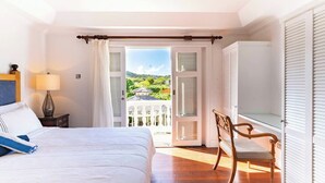 Ein Schlafzimmer mit Bett, Stuhl, Nachttisch und Blick auf einen Garten durch eine geöffnete Tür.