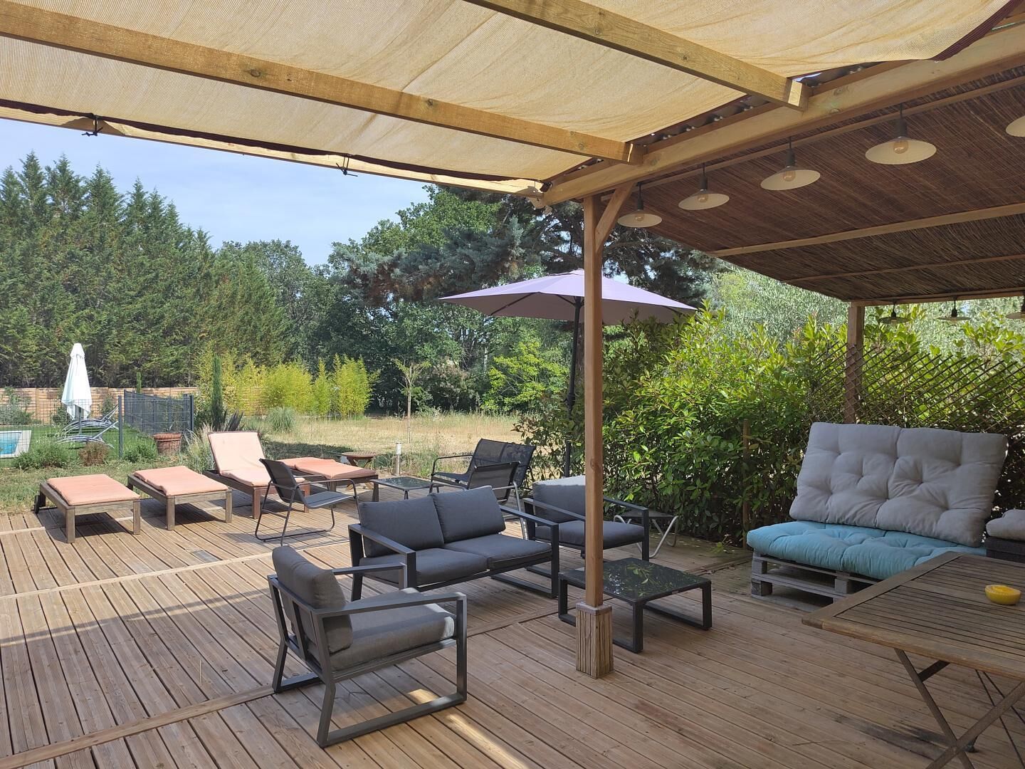 Een overdekt terras met houten vloer, lounge fauteuils en een comfortabele bank.