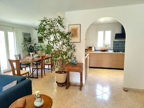 A modern living room with a dining area, a large potted plant, and a kitchen visible through an archway. - La Méridienne - Lorgues (LORGUES)