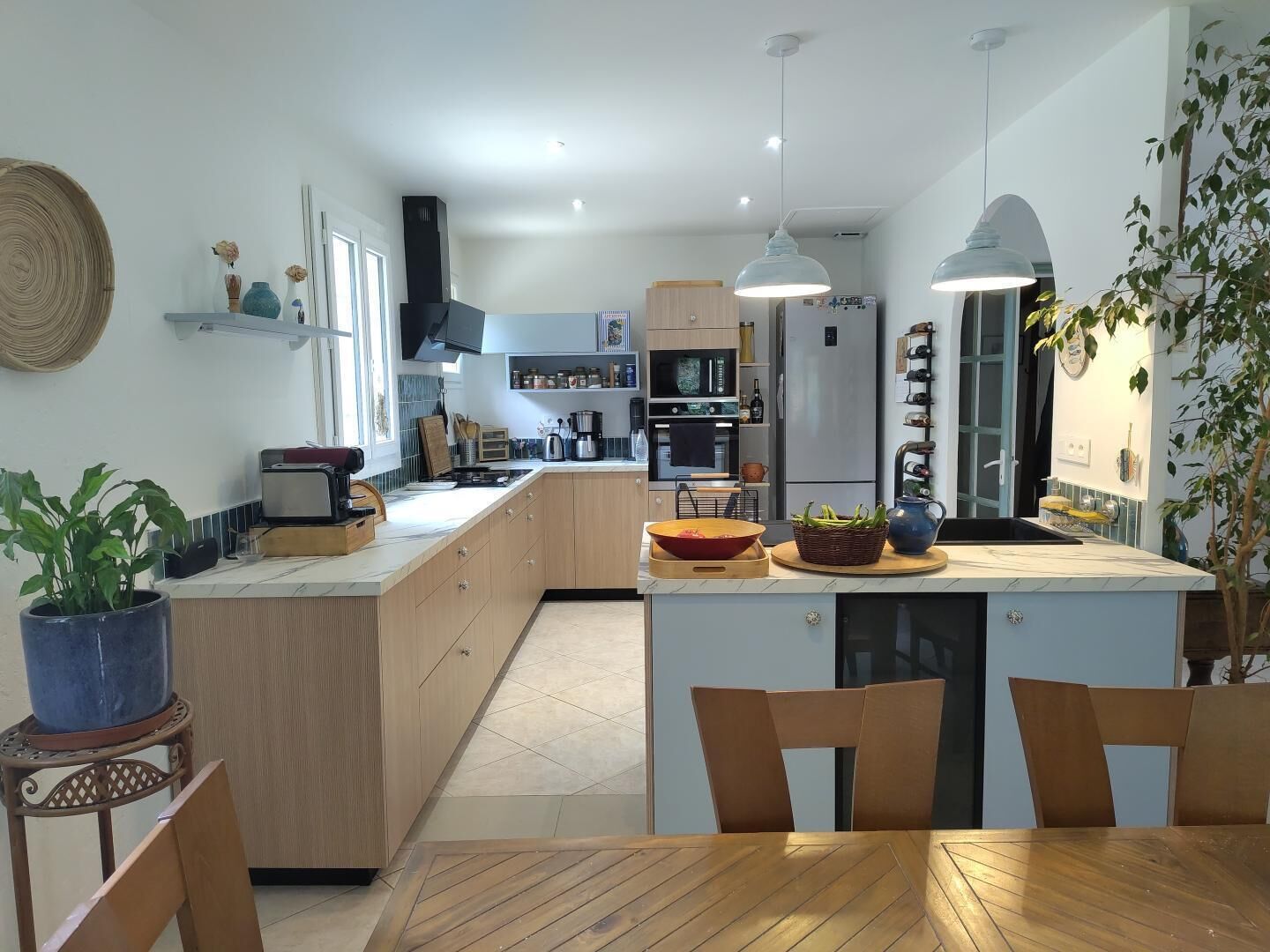 A modern kitchen with a central island, wooden cabinets, and a dining area with chairs.