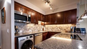 A modern kitchen with dark wooden cabinets, a stainless steel microwave, an LG washing machine, and a granite countertop. - Oceanfront, King Bed, Split AC, WiFi, Hot Tub Pool (Wailuku)