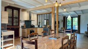 Een ruime eethoek met een grote houten tafel en stoelen, een keuken met moderne apparatuur, en uitzicht op de omgeving.