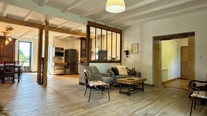 Een ruime woonkamer met houten vloeren, een bank, een salontafel, en een eethoek met een houten tafel en stoelen.