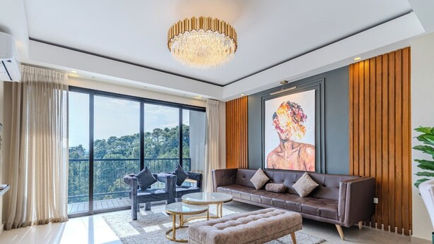 Een ruime woonkamer met een groot raam, een moderne kroonluchter, een zithoek en een schilderij aan de muur.