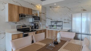 Een moderne keuken met marmeren wanden, houten kasten, roestvrijstalen apparatuur en een eethoek met een marmeren tafel en stoelen.