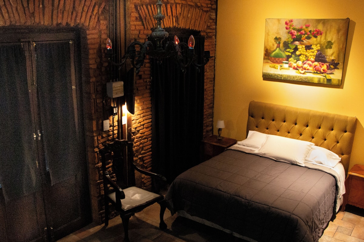 A room with a bed, a chair, a painting, and a door.