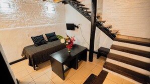 A cozy room with a sofa, a small table, a vase of flowers, a staircase, and a wall-mounted TV. - Hotel Pasaje Solar (Buenos Aires)