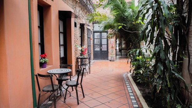 A courtyard with a tiled floor, a brick wall, and a black door. There are two tables with chairs and potted plants. - Hotel Pasaje Solar (Buenos Aires)