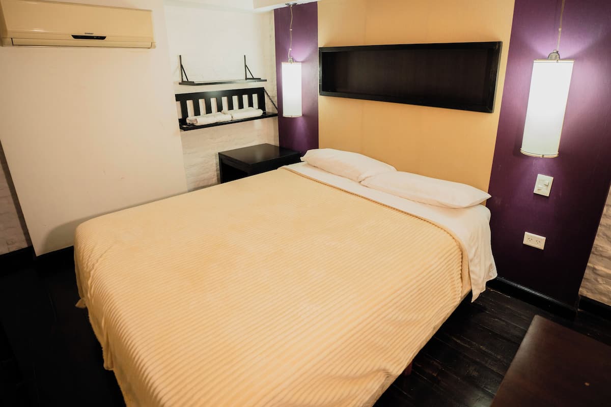A hotel room with a bed, a nightstand, a wall-mounted TV, and a wall-mounted light fixture.
