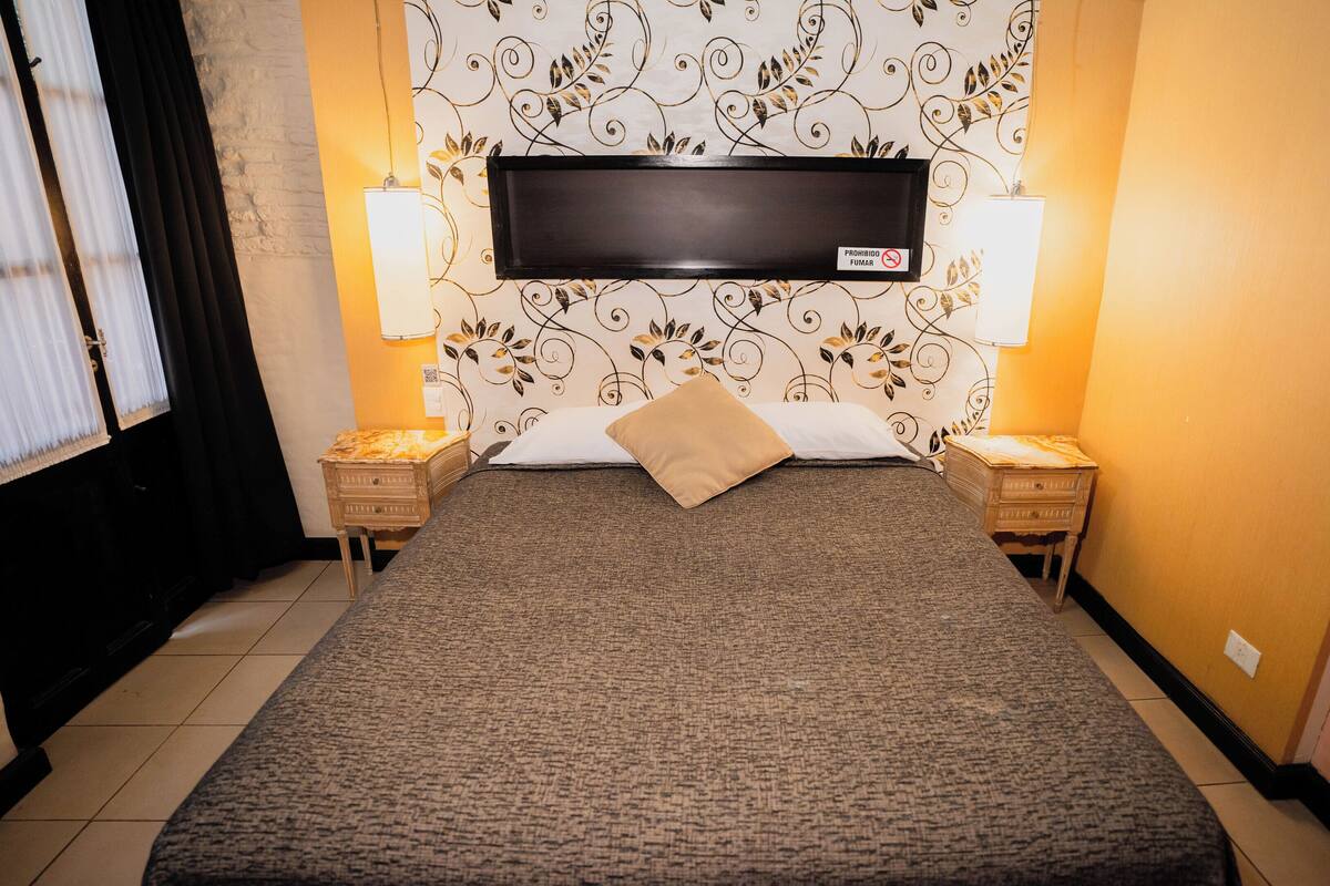 A hotel room with a large bed, two bedside tables, a wall-mounted TV, and two wall lamps.