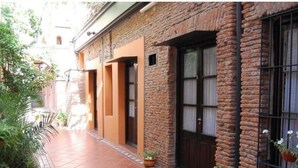 A narrow alleyway with a brick building, potted plants, and a tiled walkway. - Hotel Pasaje Solar (Buenos Aires)