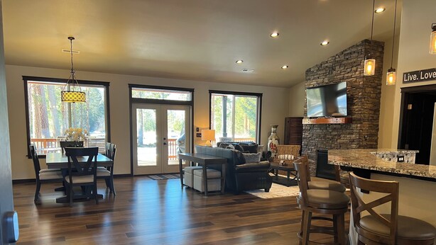 A spacious living area with a fireplace, a dining area with a table and chairs, and a kitchen with a stone accent wall and a flat-screen TV.