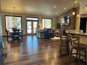 A spacious living area with a fireplace, a dining area with a table and chairs, and a kitchen with a stone accent wall and a flat-screen TV.