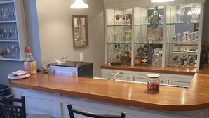 Eine Küche mit einer Holzeile, zwei Barhocker, einem Kühlschrank und einem gläsernen Schrank mit verschiedenen Flaschen und Gläsern.