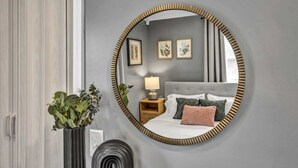 A bedroom with a round mirror, a bed with pillows, a bedside table with a lamp, and a plant. - Pool - Hot Tub - Game Room - Sleeps 8 (Ashtabula)