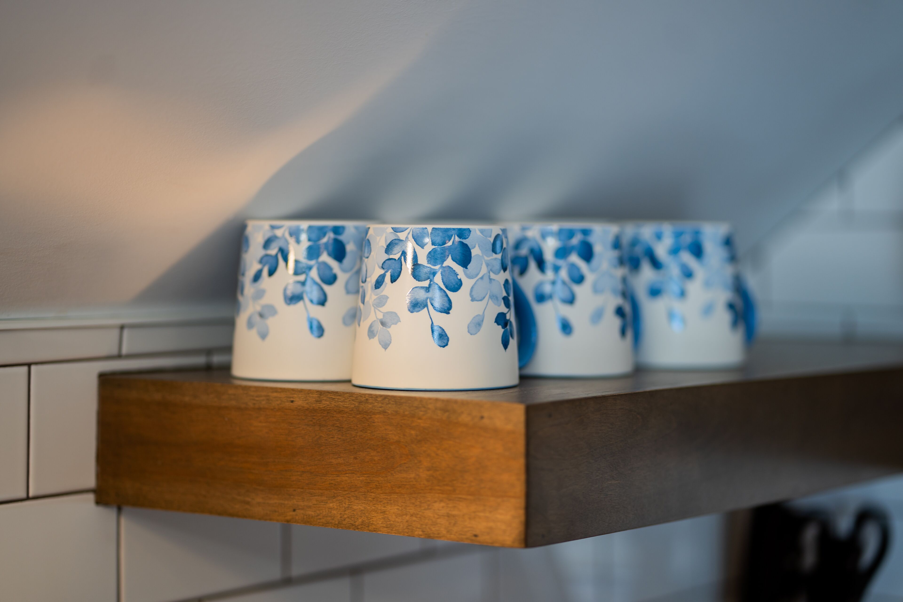 Un estante de madera con cuatro tazas blancas de cerámica decoradas con motivos florales azules.