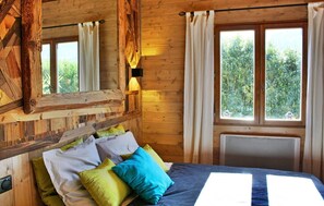 A wooden cabin room with a bed, pillows, a mirror, and a window with curtains. - Le P'Tit Chalet De La Fressine (Menthon Saint-Bernard)
