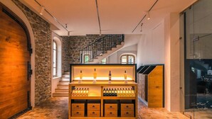 A wine cellar with wooden shelves displaying bottles, a staircase, and stone walls. - La Bastide De Cinsault (La Celle)