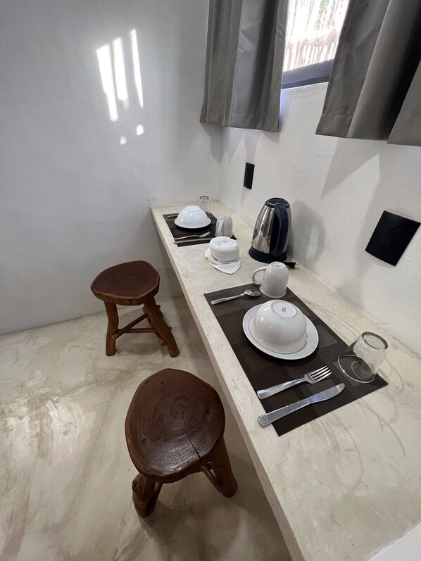 Een netjes ingerichte eethoek met een lange tafel, twee houten krukken en een waterkoker.