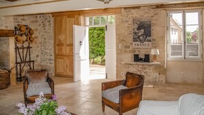 A rustic room with stone walls, wooden beams, a chandelier, a fireplace with hats, a table with a lamp, and a poster of a horse.