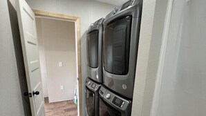 A laundry room with two stacked front-loading washers and dryers, wooden flooring, and a white door leading to another room.