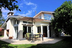 A two-story house with a patio area featuring a table and chairs, a large umbrella, and a view of the backyard. - Le Clos Daniel - Avensan (AVENSAN)