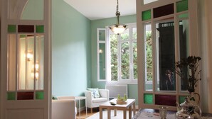 Une pièce avec un canapé blanc, une petite table, un lustre et de grandes fenêtres dotées de vitres teintées de vert.