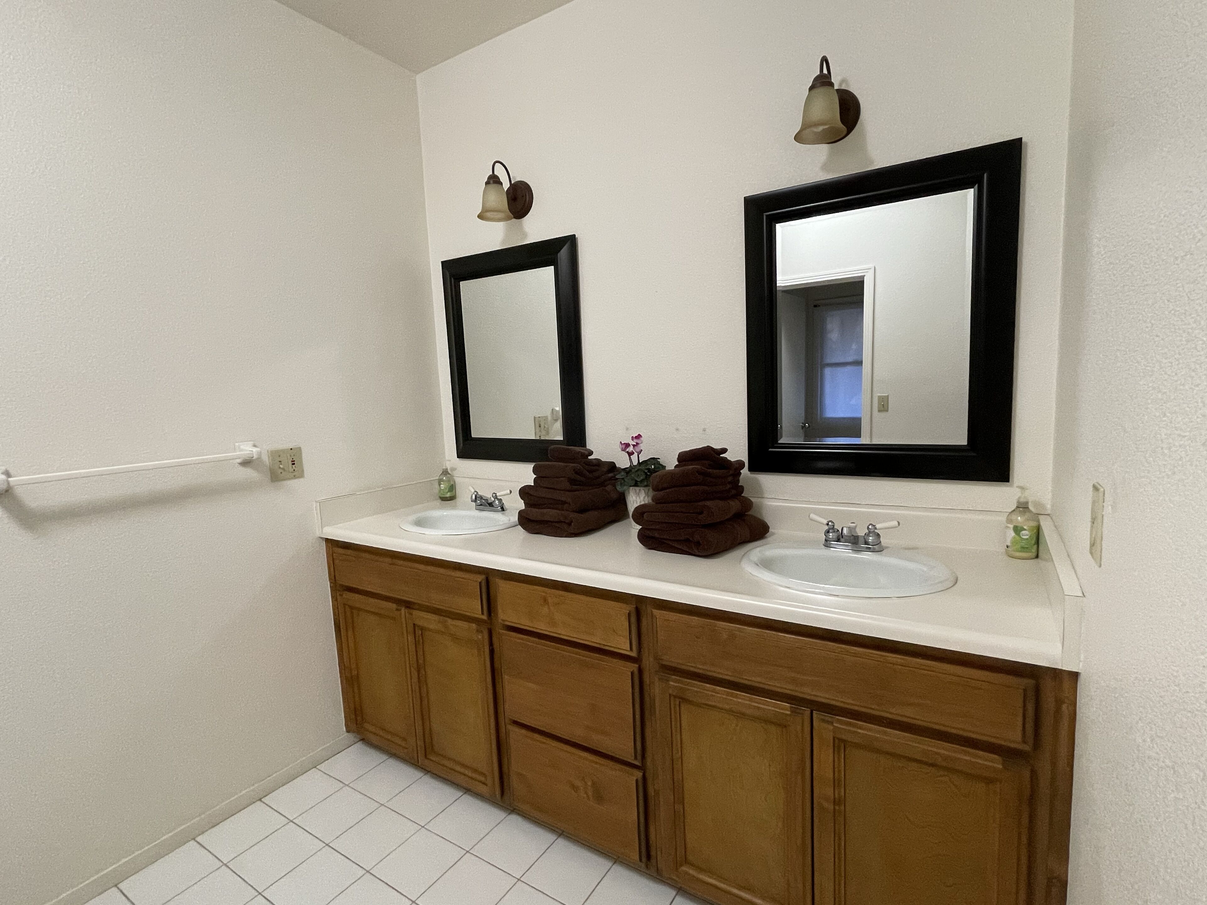 A bathroom with two sinks, a mirror, a towel rack, and wooden cabinets.
