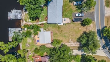 An aerial view of a residential area with a dock, a large house with a sloped roof, and a road.