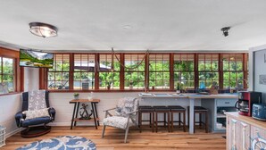 A cozy room with a wooden floor, a blue patterned rug, a comfortable chair, a small table, and a kitchen area with a coffee machine. - Waterfront on Lake Talquin - Free Kayaks - Near FSU - 2 Story Dock - Fire Pit (Tallahassee)