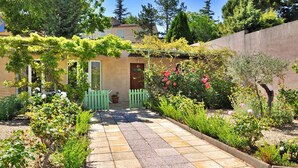A garden pathway leading to a house with a pergola covered in greenery, a wooden fence, and various flowering plants. - Les Murmures Du Ventoux (Mormoiron)