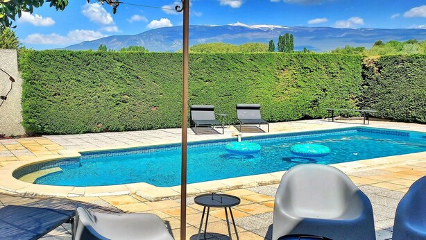 A swimming pool with lounge chairs and a table, surrounded by a hedge and a mountain view. - Les Murmures Du Ventoux (Mormoiron)