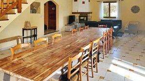A spacious dining area with a long wooden table and matching chairs, a fireplace, and a staircase. - Les Murmures Du Ventoux (Mormoiron)