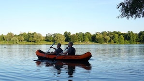 Two people in an orange inflatable boat on a calm lake with a forested shoreline in the background. - KAYAKS PERU (Tumbes)