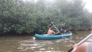 A group of people in a blue inflatable raft paddling through a river surrounded by dense mangrove foliage. - KAYAKS PERU (Tumbes)