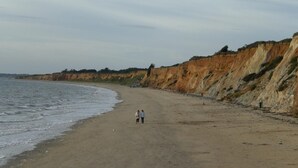 En bred sandstrand med en klippe på den ene side og rolige bølger.