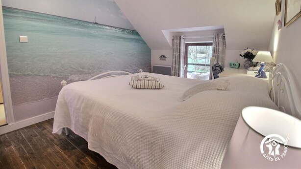 Et soveværelse med en stor seng, et natbord, en lampe og et muralmaleri af en strandscene.