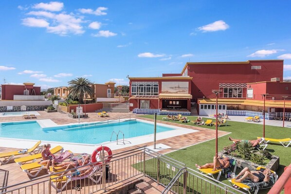 A hotel with a swimming pool, sun loungers, and a covered patio area.