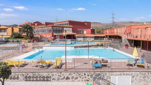 Ein Hotel mit einem zentral gelegenen Schwimmbad, Sitzgelegenheiten im Freien und einer Bergkulisse.