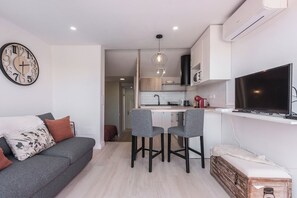 Un espacio habitable moderno con un sofá gris, una zona de cocina y un televisor montado en la pared.