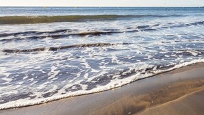 A beach with waves gently lapping onto the shore, clear skies, and distant buoys.