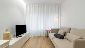 A modern living room with a flat-screen TV on a white console, a beige sofa, and a red side table.