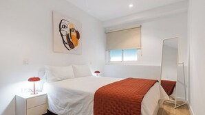 A bedroom with a bed, a nightstand, a mirror, and a window with a view.