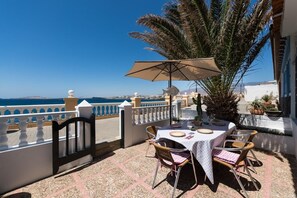 A terrace with a table set for dining, a palm tree, and a view of the sea. - Home2Book Oceanfront Bliss in Taliarte (Taliarte)