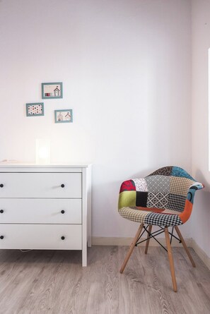 A room with a white dresser, a colorful chair, and three framed pictures on the wall.