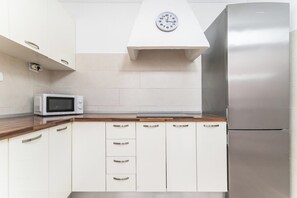 A modern kitchen with white cabinets, a stainless steel refrigerator, a microwave, and a clock on the wall.