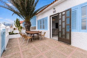 A patio with a table and chairs, a palm tree, and a building with blue shutters. - Home2Book Oceanfront Bliss in Taliarte (Taliarte)