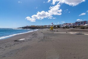 Une plage avec un poste de surveillance pour les sauveteurs, une côte rocheuse et des bâtiments en arrière-plan.